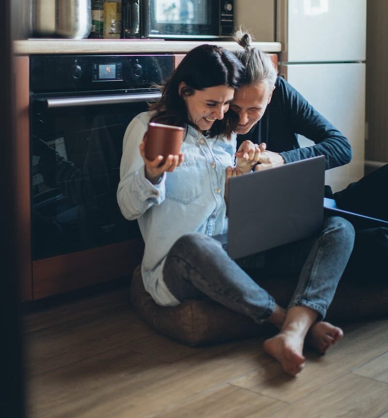 Couple Sitting on the Kitchen Floor Watching on the Laptop